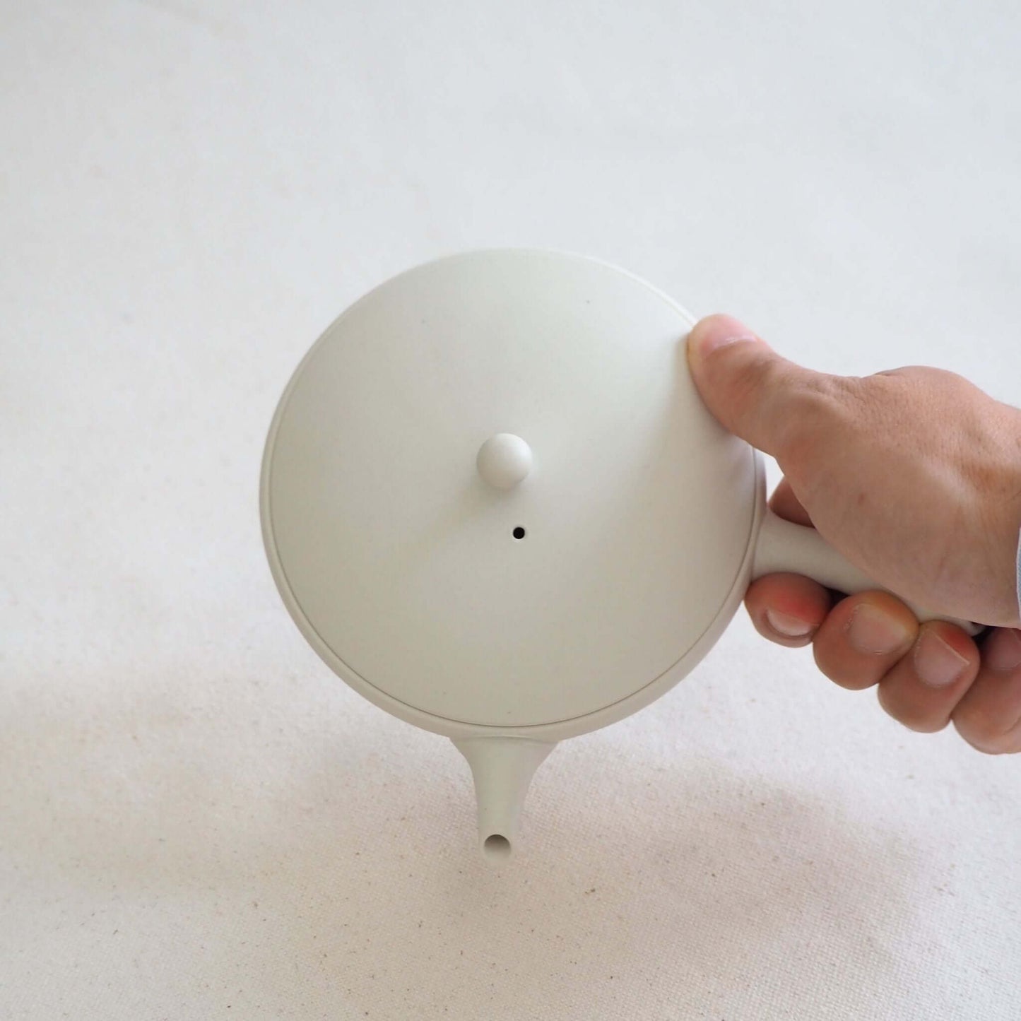 A Tokoname ware white flat teapot is held in the hand and tilted—its soft white appearance is a result of being shaped on a potter's wheel.