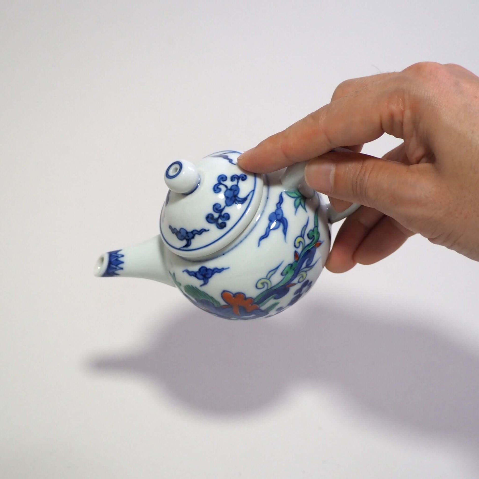He is holding and tilting a Kyo-yaki teapot with a colorful dragon design by Shoami in his hands.