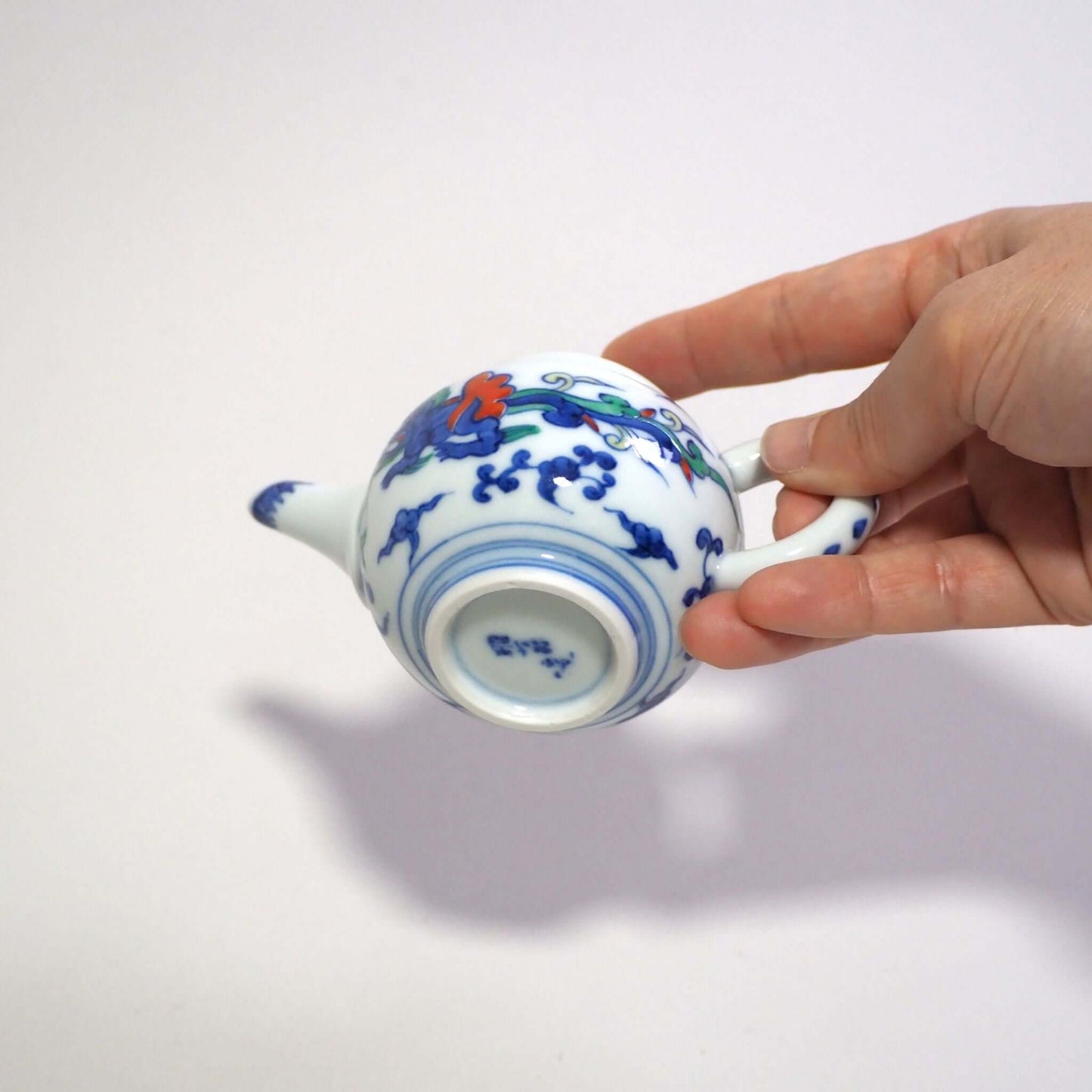 He is holding a Kyo-yaki teapot with a colorful dragon design by Shoami in his hand and looking at the bottom of the teapot.