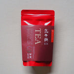 お茶のパッケージ画像です。赤色の袋に、赤茶色の紙帯で商品名が印字されています。