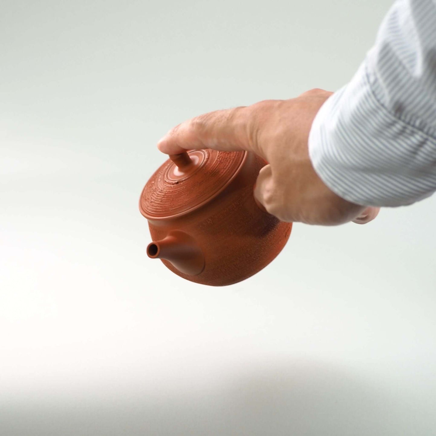 常滑焼玉光陶園の朱泥松皮急須の蓋を押さえ、急須を傾けている