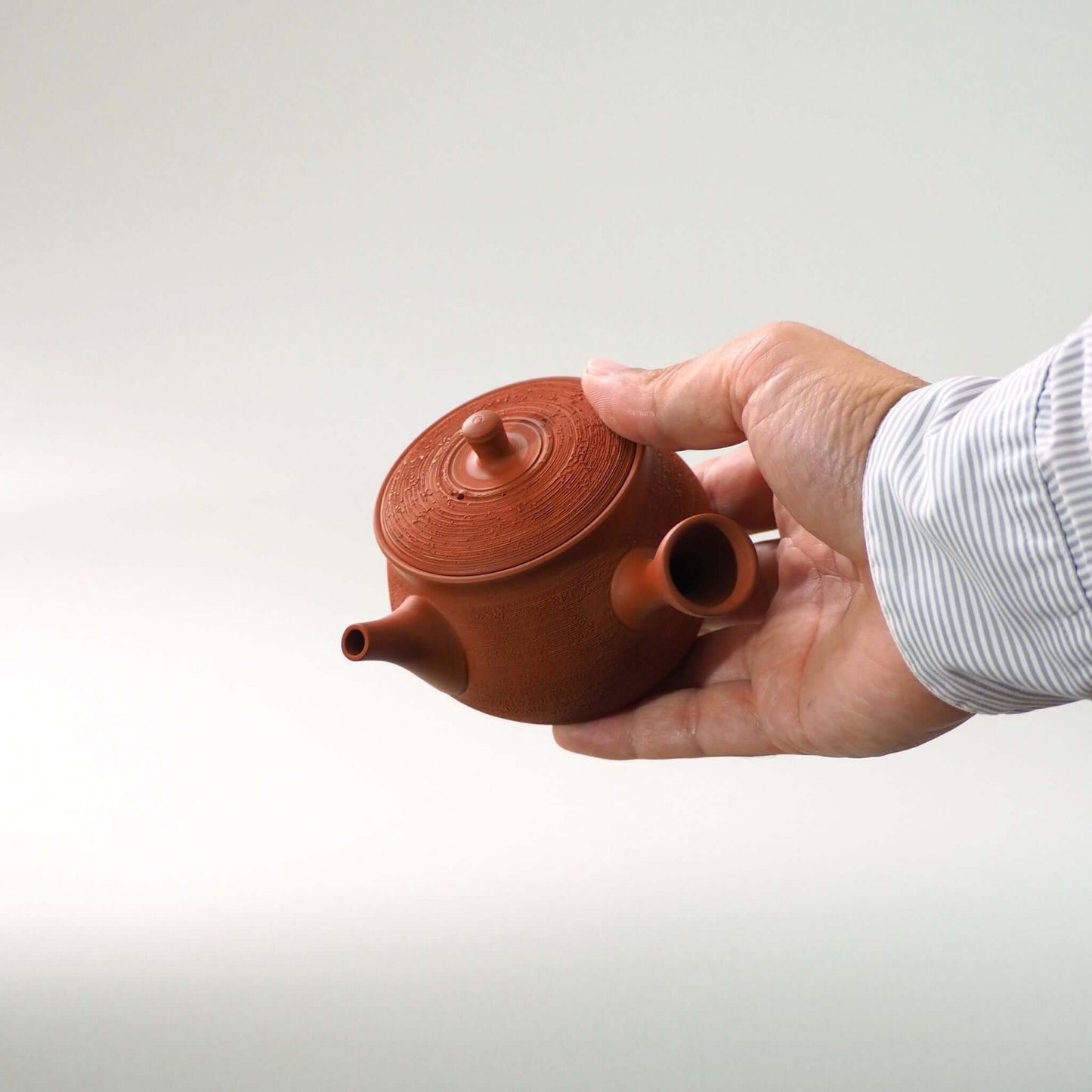 常滑焼玉光陶園の朱泥松皮急須を手で持っている
