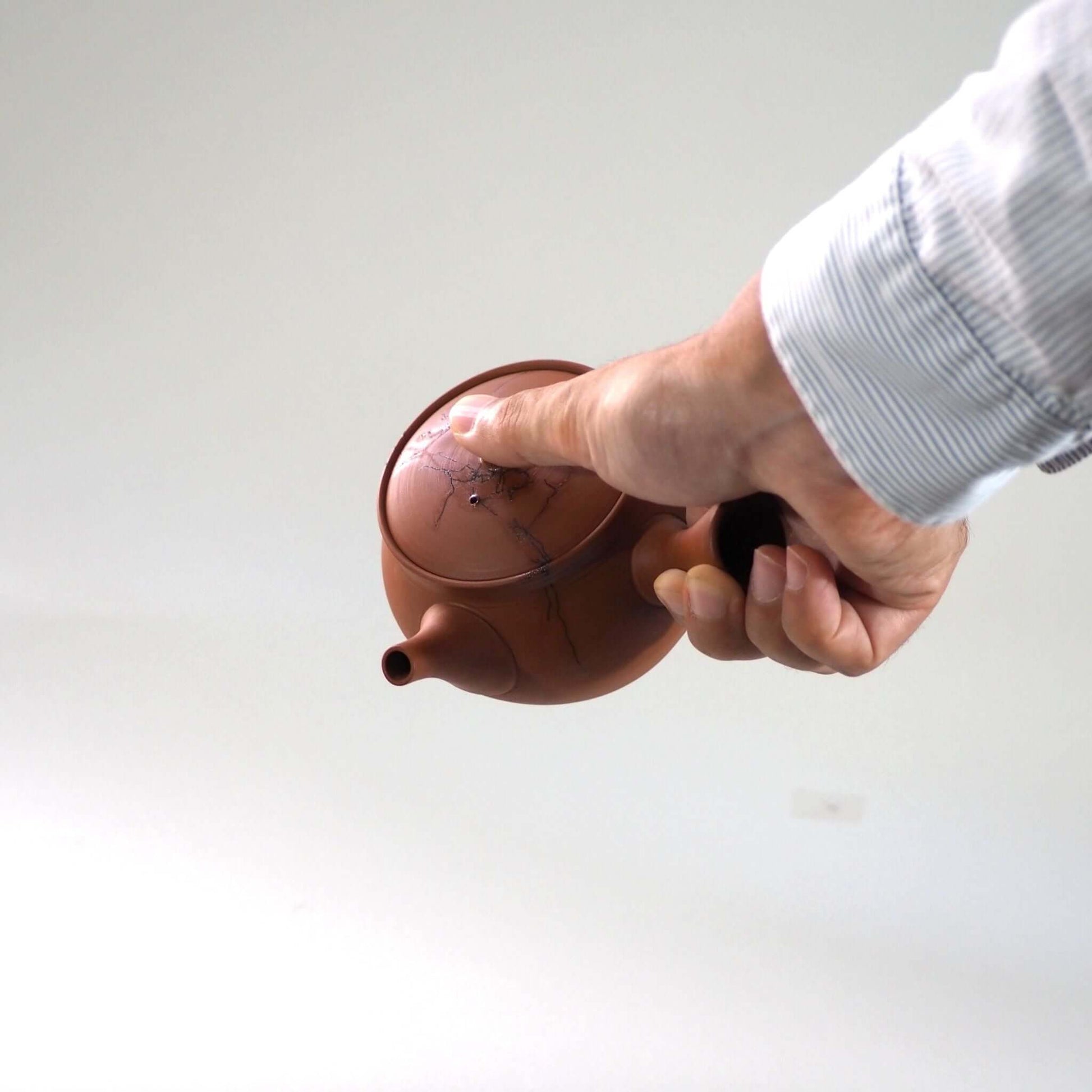 常滑焼玉光陶園の朱泥藻掛け急須を手で持ち、傾けている