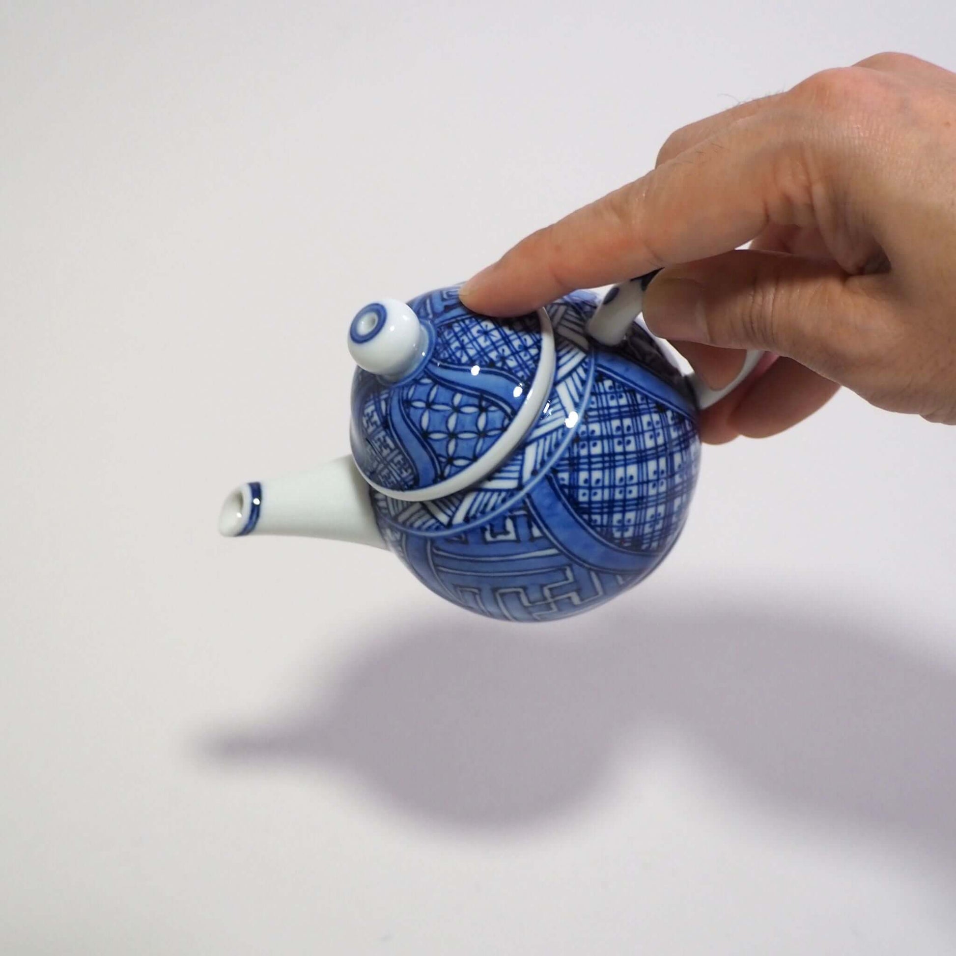 Holding a Kyo-yaki Shoami underglaze blue Shōzui teapot by hand and tilting it.