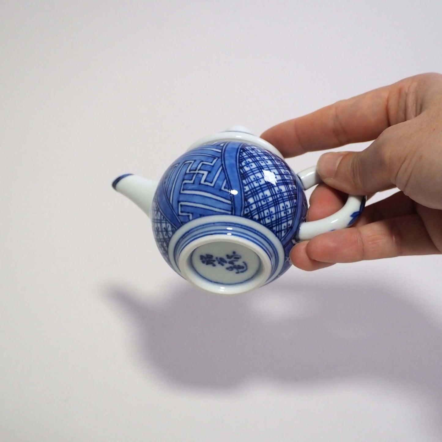 Holding a Kyo-yaki Shōami blue-and-white Shōzui teapot by hand, looking at the bottom area.