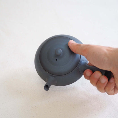 Holding and tilting a black triangular, extra-flat teapot by Tokoname ware potter Tokuta Fujita.