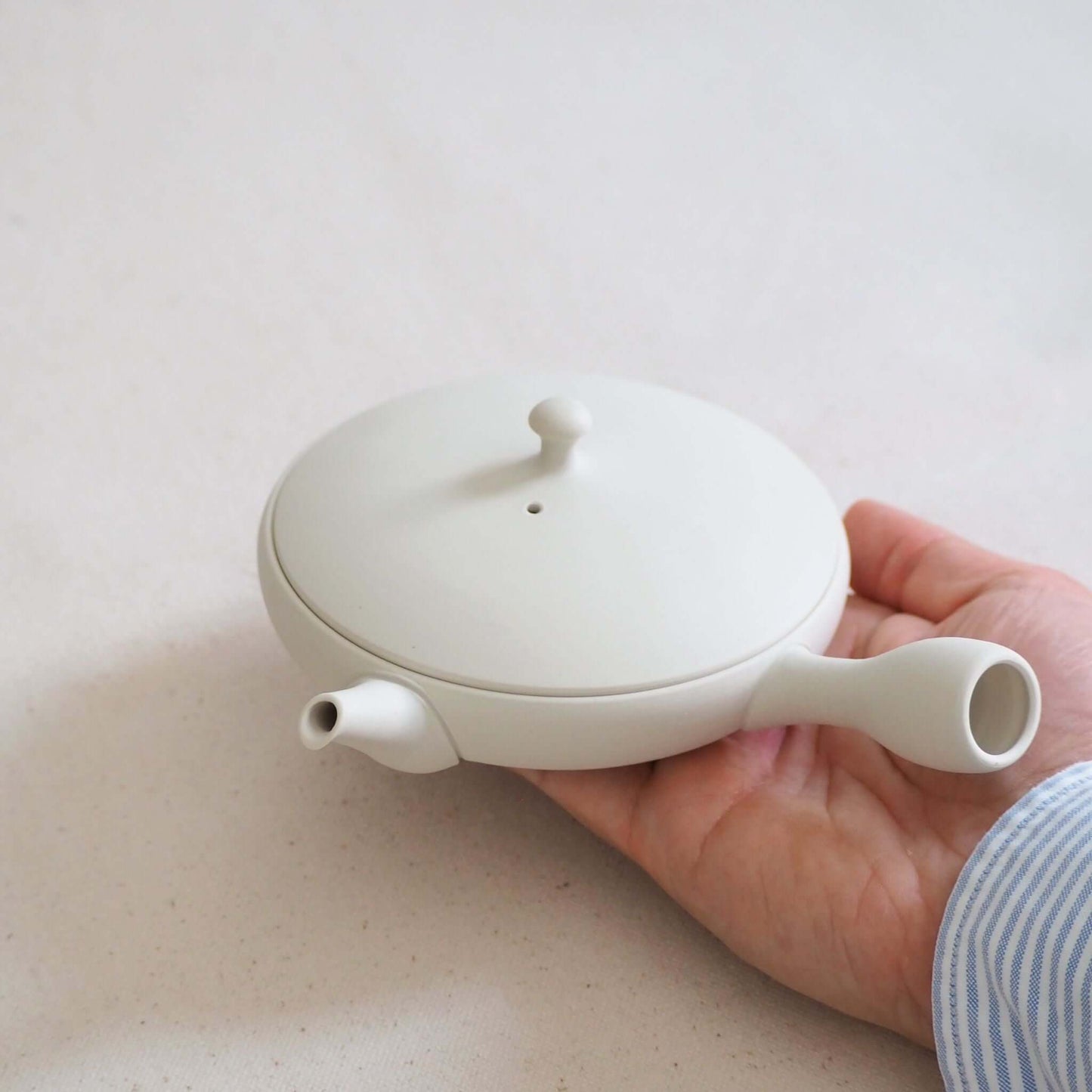 Tokoname ware white flat teapot on the hand—its soft white appearance is a result of being shaped on a potter's wheel.