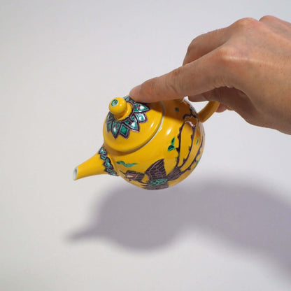 Holding and tilting a Kyo-yaki Shōami yellow-glazed phoenix teapot by hand.