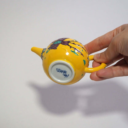 Holding a Kyoyaki Shoami yellow-toed phoenix teapot in his hand and looking at the bottom.